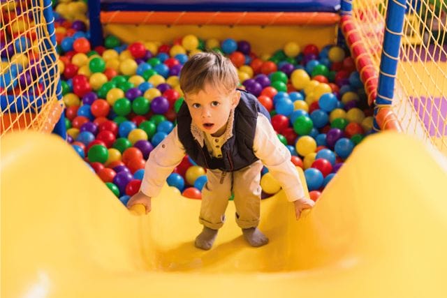 A young, adorable boy climbing up the slides in an indoor playground