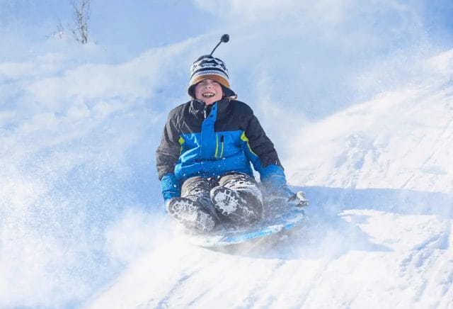 A young boy excited tobogganing down a snow hill.